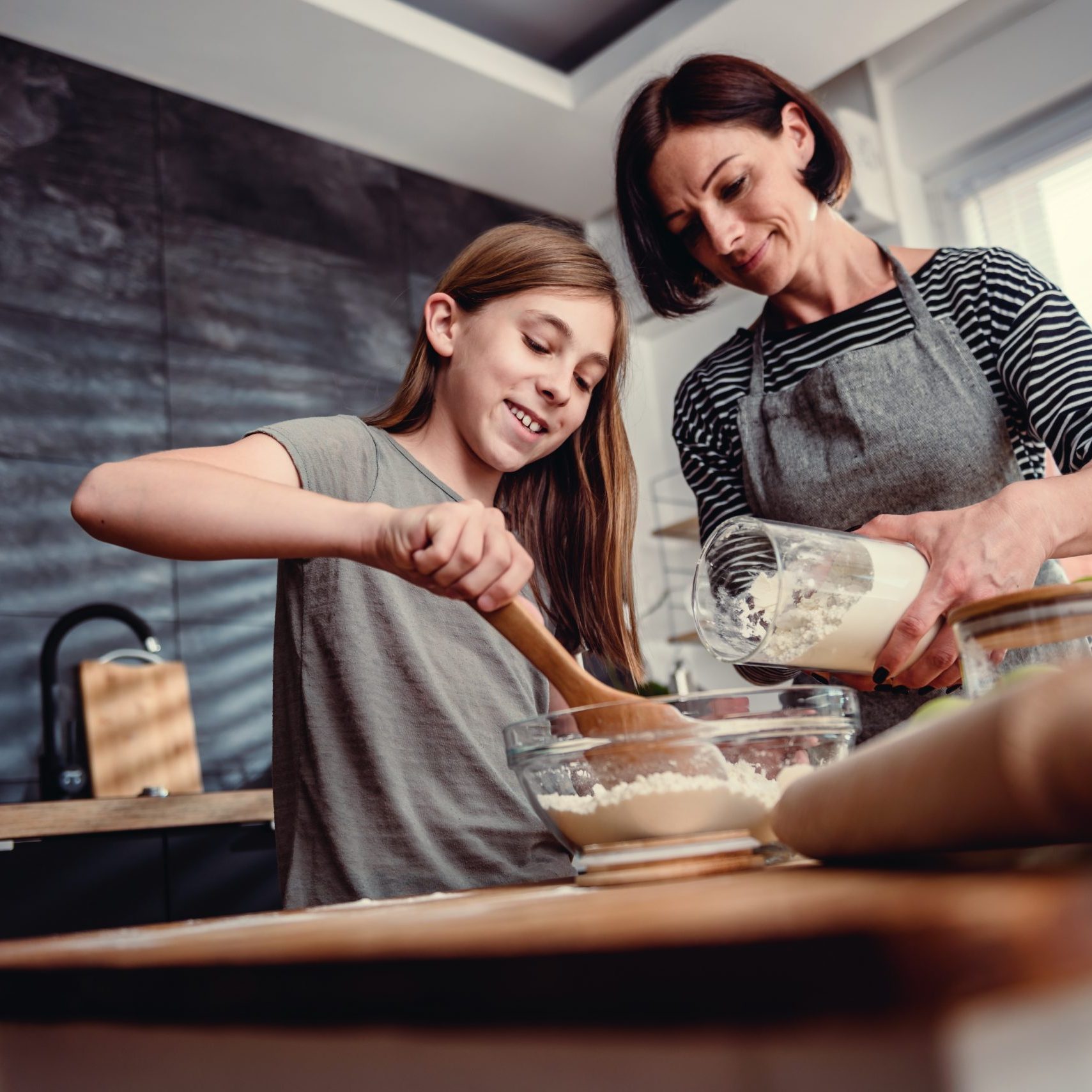 Mother and daughter making together dough for apple pie at kitchen